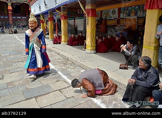 Tibetan Buddhism, woman kneeling in prayer to the religious masked Cham dance, at the important Kumbum Monastery, Gelug or Gelug-pa yellow hat sect, Ta'er Monastery, Huangzhong, Xinning, Qinghai, formerly Amdo, Tibet, China, Asia.