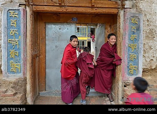 Two young novice monks, students standing in front of the entrance to a Buddhist monastery school, monastery building in the traditional architectural style, Tongren Monastery, Repkong, Qinghai, formerly Amdo, Tibet, China, Asia.