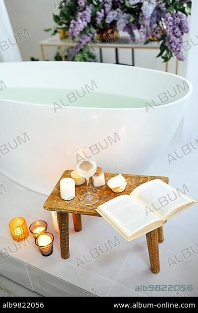 Modern bath room and spa center on the white tub wooden table. Candles and  magazine with vases with flowers. White background wall. - Album alb9821746