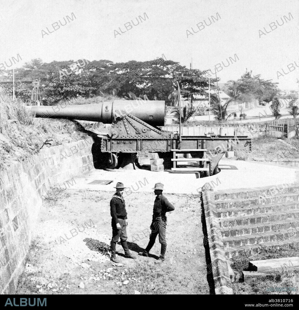 Entitled: "Modern Krupp Gun, defenses of old Manila, Philippine Islands." Showing two American soldiers standing in front of a Krupp gun. The Philippine-American War (1899-1902) was an armed conflict between the USA and Philippine revolutionaries. The conflict arose from the struggle of the First Philippine Republic to secure independence from the United States following the latter's acquisition of the Philippines from Spain after the Spanish-American War. Fighting erupted on February 4, 1899, and quickly escalated into the 1899 Second Battle of Manila. On June 2, 1899, the First Philippine Republic officially declared war against the USA. The war officially ended on July 4, 1902. The war and occupation by the USA would change the cultural landscape of the islands, as people dealt with an estimated 34,000 to 220,000 Philippine casualties, disestablishment of the Roman Catholic Church, and the introduction of the English language in the islands as the primary language of government, education, business, industrial and increasingly in future decades among families and educated individuals. Cropped stereograph card photographed by American Stereoscopic Company, October 28, 1899.