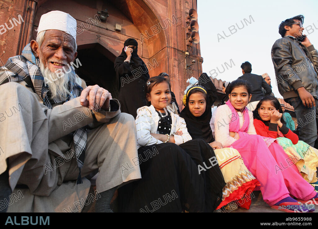 India, New Delhi, Muslim girls & their grandfather sit on the steps in front of the entrance to the Jama Masjid in the old city of Delhi.