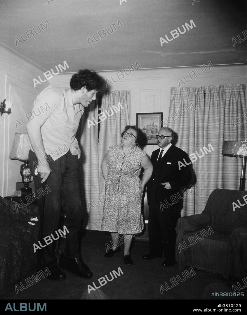 Gigantism. Giant, with his parents in their living room in 1970. Extreme cases of gigantism, like this, are usually caused by pituitary gland defects causing an excess secretion of growth hormones.