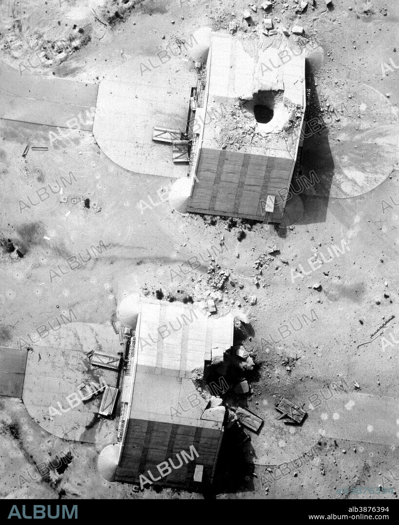 Two reinforced concrete aircraft hangars at the Ahmed Al Jaber Airfield show the results of a coalition bombing strike during Operation Desert Storm. The hangars had been suspected of housing Iraqi aircraft. The photograph was taken from a Fighter Squadron 84 (VF-84) F-14A Tomcat aircraft using the Tactical Air Reconnaissance Pod System (TARPS).