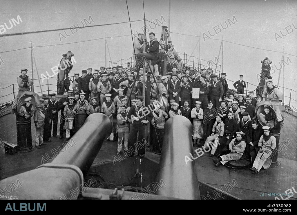 Some of the company of the first-class battleship HMS 'Sans Pareil', 1896. View showing the ship's two 16.25 inch guns, mounted in a single turret sited forward of the superstructure. Launched in 1887, the 'Sans Pareil' was the sister ship of HMS 'Victoria'. From 1895 until the end of her career in 1904, she served as port guard ship at Sheerness, Kent. A print from The Navy and Army Illustrated, 21st February 1896.