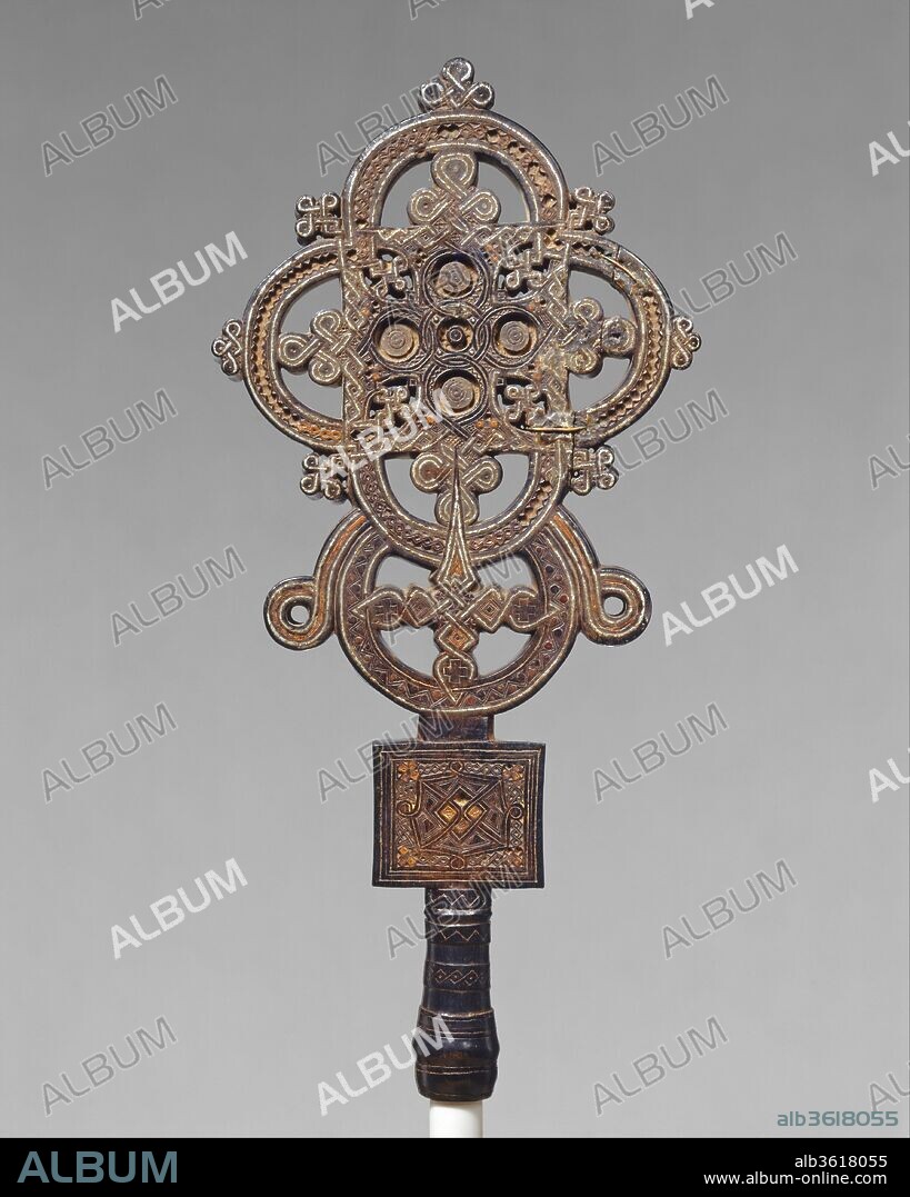 Processional Cross. Artist: Ezra. Culture: Tigrinya peoples. Dimensions: H. 18 x W. 17 in. (45.7 x  43.2cm). Date: ca. 1500.
This cross was created in the province of Tigray, near the Red Sea, the birthplace of Ethiopia's earliest kingdom and of Christianity in Africa. A small corpus of Ethiopian Christian works from before the seventeenth century has survived. 
This exceptional creation, in which a highly unusual interplay of materials affords rich tonal contrasts, is a tour de force.  The solidity of the carved-wood structure is permeated by finely applied metal inlays.  The complexity of this work, with each side elaborately distinct, is unrivaled.  It has been attributed to Ezra (ca. 1460-1522), a member of the Stephanite monastic order. The Stephanites came to be recognized as the foremost carvers of crosses and illuminators of manuscripts.  During a period of the order's exile in Egypt, Ezra is reputed to have enhanced his training as a craftsman and learned the technique of marquetry.  It has been suggested that he may have produced this work at the Gunda Gunde monastery, renowned for its manuscripts.
In the Ethiopian church, the wooden cross is perceived as having been sanctified by Christ's blood, which conferred upon it infinite power to heal and to bless. Foliate and organic interlace designs, branching from the foot of the cross, are interpreted as symbolizing the Tree of Paradise, and thus a vibrant life-giving force. Commissioned by Ethiopian royalty, such works were presented to important monasteries to be carried in liturgical processions.