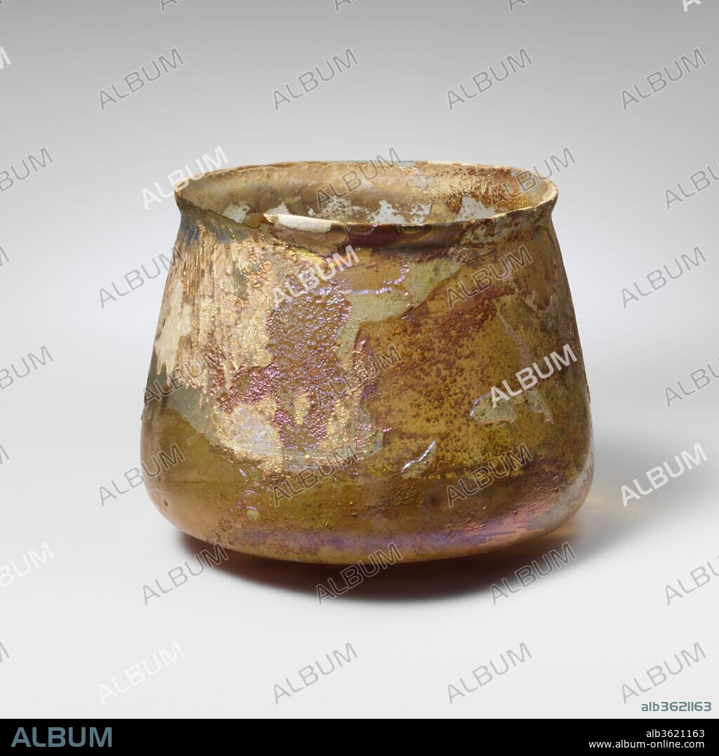 Glass cup. Culture: Roman. Dimensions: Height: 2 3/4 in. (7 cm)
Diameter: 3 1/2 x 2 7/8 in. (8.9 x 7.3 cm). Date: 2nd-3rd century A.D..
Colorless with pale greenish tinge.
Knocked-off, uneven rim; slightly bulging collar below rim; sides expanding downward, then angled in to join convex bottom, flattened at center.
Band of two faint wheel-cut lines on body above angle.
Intact, except for weathered chip in rim; some bubbles; dulling, deep pitting, and brilliant iridescent weathering.