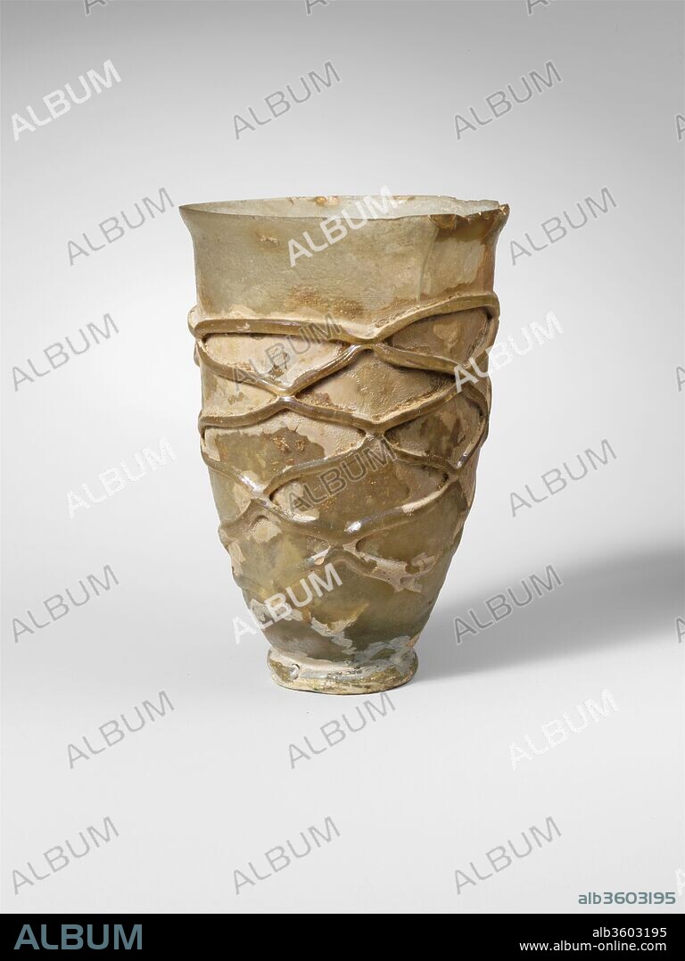 Glass beaker. Culture: Roman. Dimensions: H.: 3 5/8 in. (9.2 cm)
Diam.: 2 1/2 x 1 1/8 in. (6.4 x 2.9 cm). Date: late 2nd-3rd century A.D..
Colorless, with same color trail and foot ring.
Knocked-off rim; slightly bulging collar below rim; side tapering downward; applied coil foot ring; kick in bottom.
Thick trail wound six times in a spiral down body and tooled to form irregular lozenge or network pattern.
Intact, except for very chips and crack in rim; pinprick bubbles; dulling, severe pitting, iridescence, and creamy weathering.