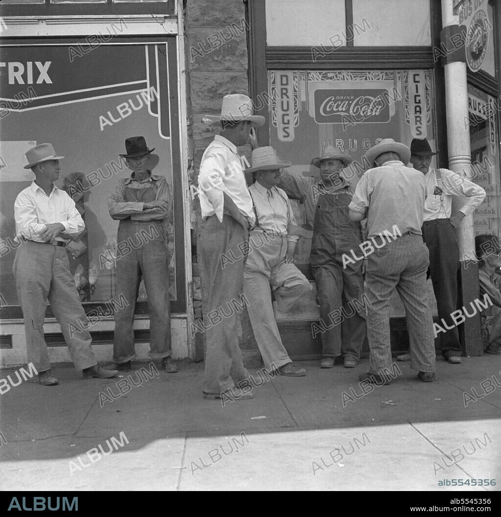 DOROTHEA LANGE. Drought farmers line the shady side of the main street on the town while their crops burn up in the fields. "Hello Bill, when's it gonna rain?".