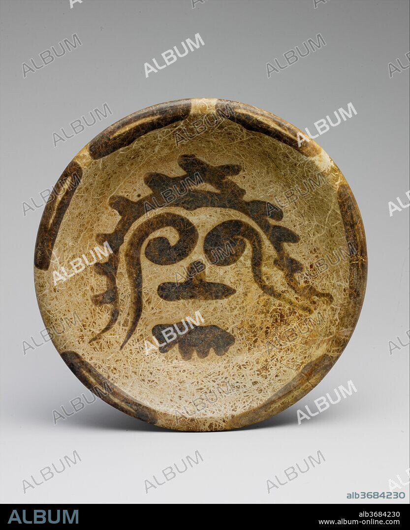 Tripod Plate. Culture: Maya. Dimensions: H. 2 1/2 x Diam. 10 7/8 in. (6.4 x 27.6 cm). Date: 9th-10th century.
Referred to by archaeologists as slateware, this ceramic vessel is a variety that was especially popular in northern Yucatan in the centuries around the turn of the second millennium A.D. The subdued colors of slateware, ranging from pale beige-whites to soft grays, are in marked contrast to the vibrant Maya polychrome ceramics of earlier times. As in this example, the decoration is often restrained. The image that adorns the inner surface of this tripod plate recalls the Mesoamerican rain deity with his round goggle eyes and toothy mouth. Applied with a fluid, spontaneous brushstroke, the viscosity of the "trickle" paint causes it to run when first applied, contributing to the organic nature of the painted motif.