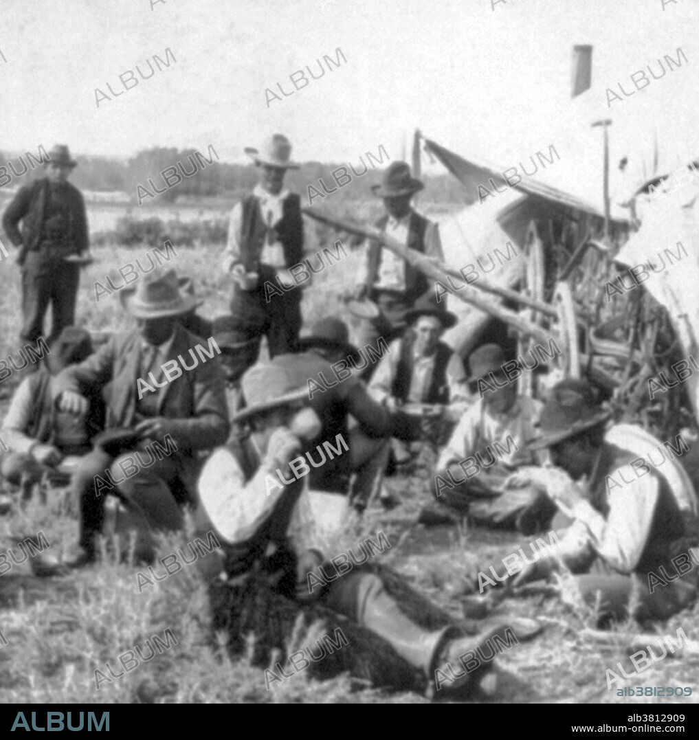 The chuckwagon is attributed to Charles Goodnight, a Texas rancher, who introduced the concept in 1866. Cattlemen herded cattle in parts of the country that did not have railroads which meant they needed to be fed on the road for months at a time. Goodnight modified the Studebaker wagon, a durable army-surplus wagon, added a "chuck box" to the back of the wagon with drawers and shelves for storage space and a hinged lid to provide a flat cooking surface. A water barrel was also attached to the wagon and canvas was hung underneath to carry firewood. A wagon box was used to store cooking supplies and cowboys' personal items. Chuckwagon food typically included easy-to-preserve items like beans and salted meats, coffee, and sourdough biscuits. Food would also be gathered en route. There was no fresh fruit, vegetables, or eggs available and meat was not fresh unless an animal was injured during the run and therefore had to be killed. The meat they ate was greasy cloth-wrapped bacon, salt pork, and beef, usually dried, salted or smoked. The wagon was also stocked with a water barrel and a sling to kindle wood to heat and cook food. Photographed by Keystone View Company, 1905.