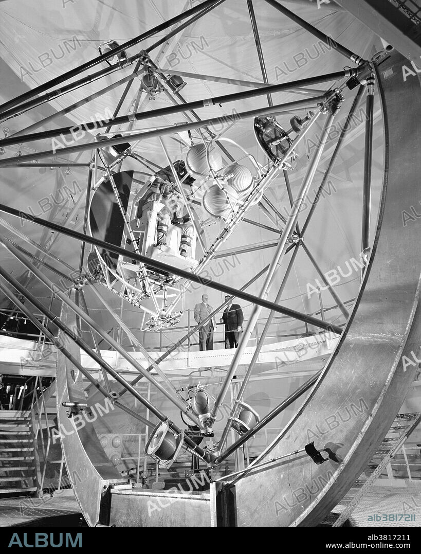 The MASTIF, or Multiple Axis Space Test Inertia Facility, was installed at the Altitude Wind Tunnel at the Lewis Research Center, now John H. Glenn Research Center. Three tubular aluminum cages could revolve separately or in combination to give roll, pitch and yaw motions at speeds up to 30 revolutions per minute, greater than those expected in actual space flight. Nitrogen-gas jets, attached to the three cages, controlled the motion. NASA engineers built the entire rig inside a test chamber in the research center's old Altitude Wind Tunnel. At the center of the innermost cage, the pilot was strapped into a plastic seat, similar to that in the Mercury capsule. His head, body and legs were held in place, leaving only his arms free. The pilot actuated the jets by means of a right-hand control column. Communication was by radio, which was operated by a button atop the left-hand column. An operator at the control station started the complex tumbling motions, and then switched control to the pilot. By reading instruments mounted at eye level before him, the pilot interpreted his motions and made corrections accordingly. A movement of the column to the right or the left fired the nitrogen-gas jets on the roll cage. In a similar manner, forward or backward movement of the column fired the jets on the pitch cage, and twisting movements actuated jets on the yaw cage. NASA photograph October 29, 1959.