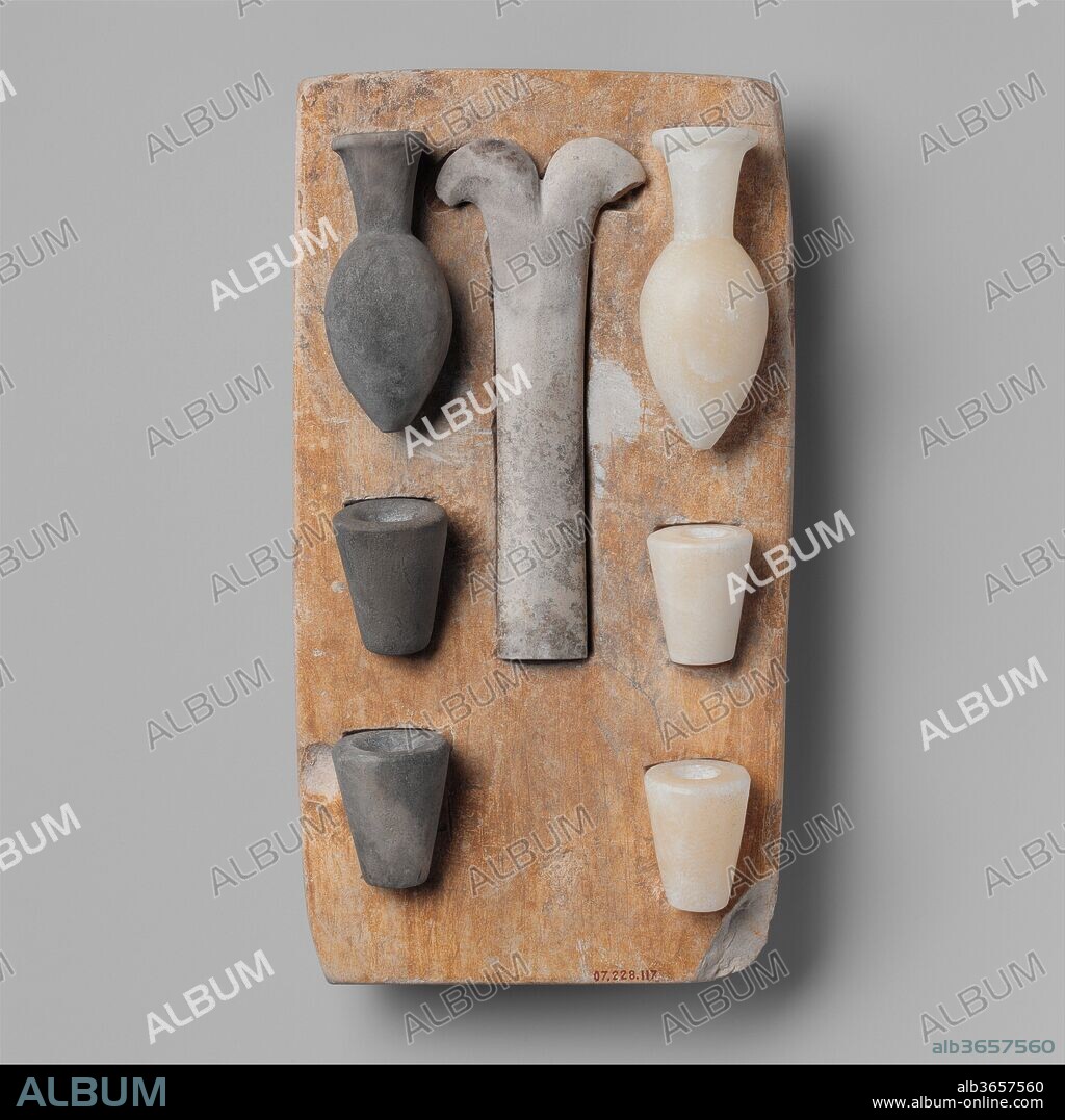 Model of the "Opening of the Mouth" ritual equipment. Dimensions: Tray: L. 22 × W. 12 × H. 3.2 cm (8 11/16 × 4 3/4 × 1 1/4 in.). Dynasty: Dynasty 5-6. Date: ca. 2465-2150 B.C..
The small stone tray holds models of objects required for the Opening of the Mouth ceremony. This rite reanimated the deceased or animated a statue so that it could eat, breathe, see, hear, and otherwise enjoy everything offered to it. 
The forked instrument was touched to the mouth of the deceased's mummy or statue;  it symbolically restored the individual's capability of independent existence. In addition to the implement, this set includes replicas of the vessels with which the newly revived spirit was offered milk (a baby's first source of nourishment), salt water (used for cleansing), and fresh water..
Forked blades (see 16.2.6) were included in burials throughout the Predynastic Period.The cutting edge is the V-shaped notch. Although the implement's exact purpose is unknown, there is persuasive evidence that it was used at birth to cut the umbilical cord and was placed in the grave to assist its owner's rebirth into the afterlife.