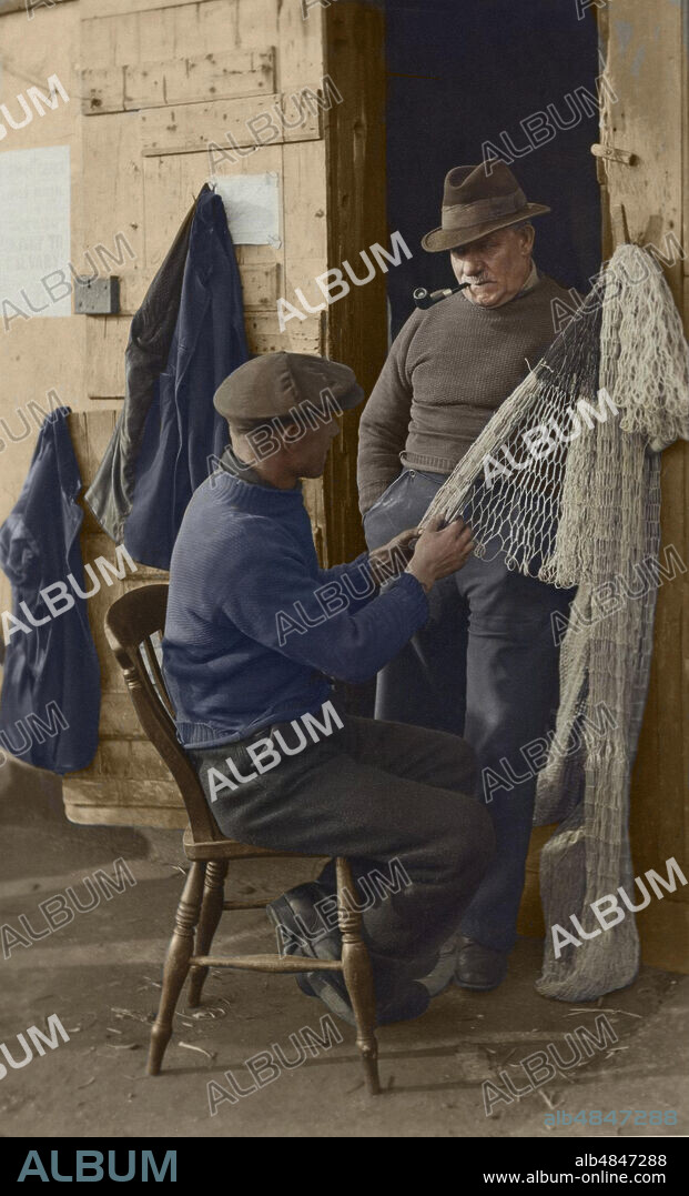 Postcard circa 1923, Victorian / Edwardian, social history. A Judges  Postcard from 'Mending nets', two fishermen in a doorway, one sitting  mending fishing nets and the oth - Album alb4847288