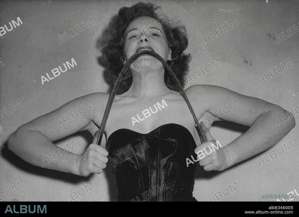 Britain's Strong-Arm Girl -- Miss Joan Rhodes shows how she bends a steel bar with her teeth, demonstrating the tremendous power of her jaw and neck muscles.
Probably the strongest girl in Britain to-day is Miss Joan Rhodes, who recently amazed "viewers" with her feats of strength before the television cameras of the B.B.C.
Miss Rhodes thinks nothing of tearing thick telephone directories in half with her hands or bending steel bars with her teeth, besides lifting two or three times her own weight.
Joan is just "naturally strong" and apart from ordinary sports such as swimming, tennis etc, has never had any special physical training.  March 14, 1950. (Photo by Sport & General Press Agency, Limited).