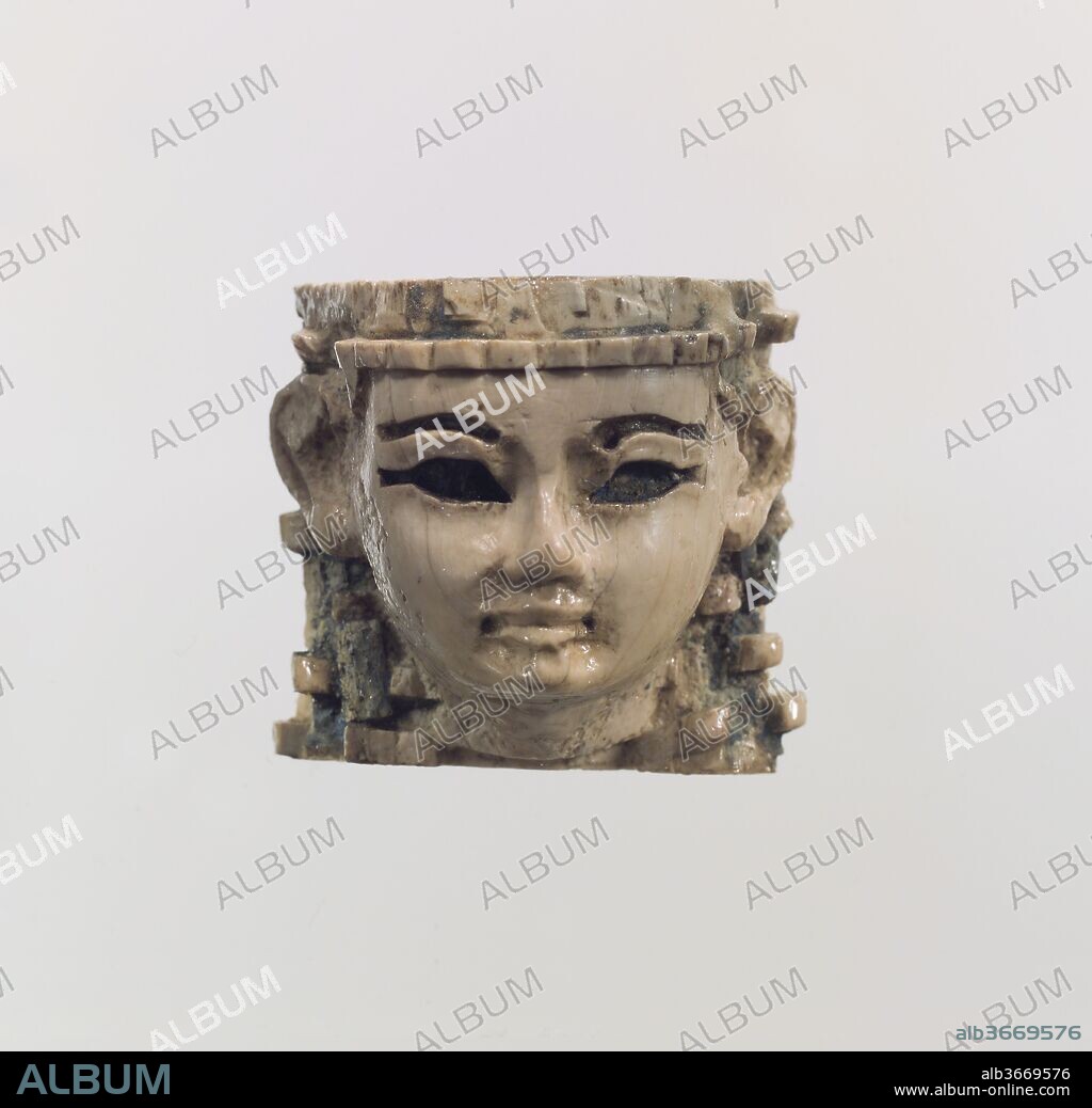 Head of a male or female figure. Culture: Assyrian. Dimensions: 1.02 x 1.14 in. (2.59 x 2.9 cm). Date: ca. 9th-8th century B.C..
This small ivory head is beardless and its gender cannot be securely determined. It was found in a room at Fort Shalmaneser, a royal building at Nimrud that was probably used to store tribute and booty collected by the Assyrians while on military campaign. Originally, the head may have been part of a composite statuette, made of various materials and painted or overlaid with gold foil. The top and reverse have been roughened, probably to help glue join the surface of the ivory to another piece made out of wood or ivory that comprised the upper part and back of the head. The soft modeling and use of inlays, now missing, in the deeply cut eyes and eyebrows are characteristic of Phoenician ivories. The wig is tied by knots at intervals and preserves some of its original inlay of Egyptian blue, a vibrant artificial pigment made of silica, lime, copper, and alkali. Another Phoenician-style ivory head found at Nimrud is also in the Metropolitan Museum's collection (MMA 62.269.2).
Built by the Assyrian king Ashurnasirpal II, the palaces and storerooms of Nimrud housed thousands of pieces of carved ivory. Most of the ivories served as furniture inlays or small precious objects such as boxes. While some of them were carved in the same style as the large Assyrian reliefs lining the walls of the Northwest Palace, the majority of the ivories display images and styles related to the arts of North Syria and the Phoenician city-states. Phoenician style ivories are distinguished by their use of imagery related to Egyptian art, such as sphinxes and figures wearing pharaonic crowns, and the use of elaborate carving techniques such as openwork and colored glass inlay. North Syrian style ivories tend to depict stockier figures in more dynamic compositions, carved as solid plaques with fewer added decorative elements. However, some pieces do not fit easily into any of these three styles. Most of the ivories were probably collected by the Assyrian kings as tribute from vassal states, and as booty from conquered enemies, while some may have been manufactured in workshops at Nimrud. The ivory tusks that provided the raw material for these objects were almost certainly from African elephants, imported from lands south of Egypt, although elephants did inhabit several river valleys in Syria until they were hunted to extinction by the end of the eighth century B.C.