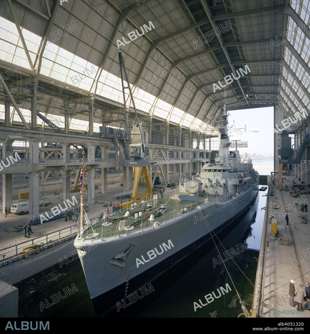 HMS 'Cleopatra' at Devonport frigate complex, Plymouth, Devon, 1977. The Devonport frigate complex was completed in 1977 and continues to provide a covered refitting facility for frigates and destroyers. In the photograph, HMS 'Cleopatra' (F28) births in the covered dock. The ship was built at Devonport and launched in 1964, joining the Beira Patrol, which prevented oil from reaching landlocked Rhodesia via the then Portuguese colony of Mozambique. The 'Cleopatra' aslo took part in the fleet review for the Queen's Silver Jubilee in the year the photograph was taken. By the early 1980s, the frigate was starting to show its age and was decommisioned on 31st January 1982 and was sold for scrap the following year.