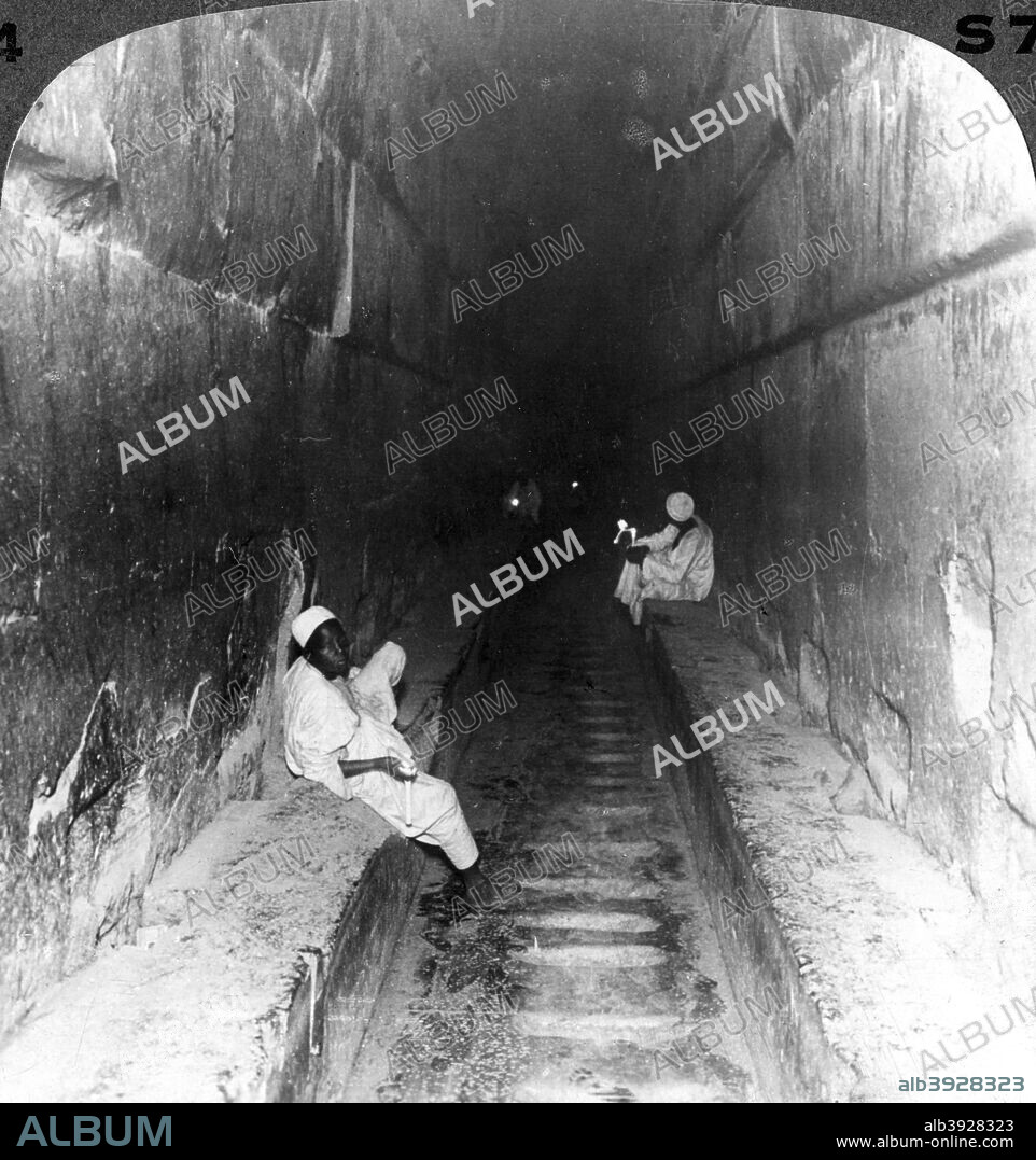 'Looking down the main passage to Khufu's sepulchre within the Great Pyramid, Egypt', 1905. 'Up this superb hall the body of the king was borne on the day of burial; those cuttings in the side walls just above the ramps were probbly for the reception of timbers intended to facilitate the ascent. The chamber behind us, in which the body was to rest, is no less remarkable than the grand hall down which we look.' Stereoscopic card. Detail. From a series called Egypt Through the Stereoscope, text by James H Breasted.