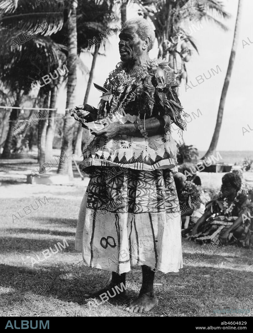 Fiji, Fijian man with a 'tabua'A Fijian man wearing face paint and ceremonial costume made from 'masi' (bark cloth) holds a 'tabua' (polished whale's tooth) in one hand. The tabua is an important cultural item in Fijian society, which was traditionally given as a gift of atonement or esteem. Caption reads: In ancient times 'Tabua' (whales' teeth) had a power far above their intrinsic worth, and were often the price of life or death, the indispensible adjunct to proposals of marriage, alliance, intrigue, request, apology, appeal to the gods or sympathy with the bereaved. Tabua were stained, oiled, polished and fitted with plaited cords by which they were handled. Today they are reserved for ceremonial occasions for the visits of distinguished people to the colony, 1965. 2005/010/1/14/49.