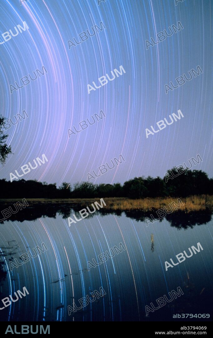 Star trails in the Southern Hemisphere sky at 19 degrees south latitude, Okavango Delta, Botswana, with reflection in lagoon. The direction is southwest. Taken from 8:15 p.m. to 1:45 a.m. on June 19-20, 1993.