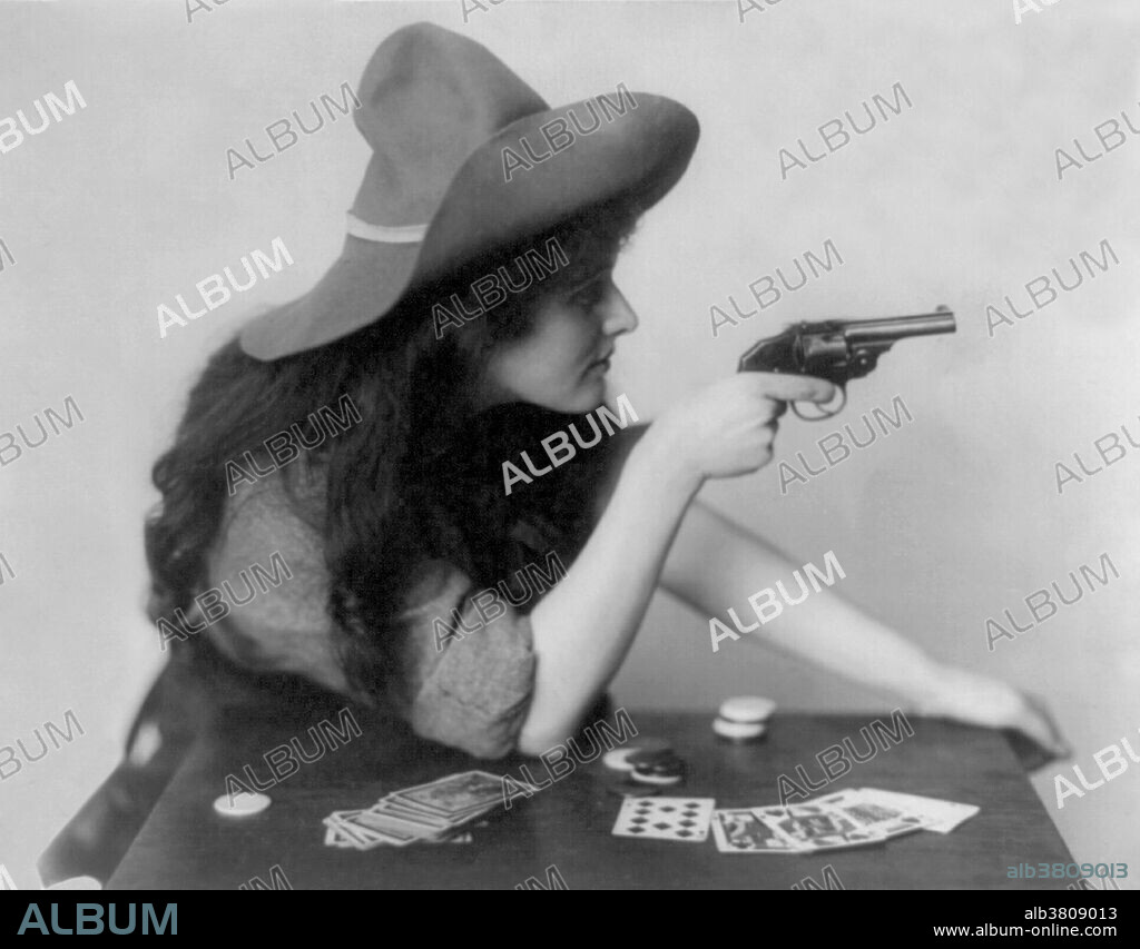 Woman in cowgirl clothing, seated at table with deck of cards and chips, pointing pistol, with arm on table. The history of women in the west, and women who worked on cattle ranches in particular, is not as well documented as that of men. It wasn't until the advent of Wild West Shows that "cowgirls" came into their own. These adult women were skilled performers, demonstrating riding, expert marksmanship, and trick roping that entertained audiences around the world. Women such as Annie Oakley became household names. By 1900, skirts split for riding astride became popular, and allowed women to compete with the men without scandalizing Victorian Era audiences by wearing men's clothing or, worse yet, bloomers. In the movies that followed from the early 20th century on, cowgirls expanded their roles in the popular culture and movie designers developed attractive clothing suitable for riding Western saddles. Photographed by Celebrity Art Company, 1912.