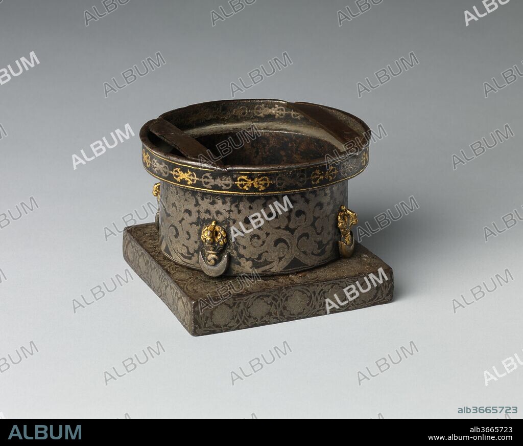 Base from a Purification Brazier. Culture: Tibet, probably Derge. Dimensions: H. 3 5/16 in. (8.4 cm); W. 4 9/16 in. (11.6 cm); Diam. 4 3/4 in. (12.1 cm). Date: 15th-17th century.
This brazier was used for burning sacrificial offerings during purification rites. The circle-on-a-square configuration is echoed in the fire-offering ladles displayed nearby. The base and the drum display a meandering lotus-flower decoration, the drum with four flaying knives in high relief. All the gold and silver decoration is damascened.