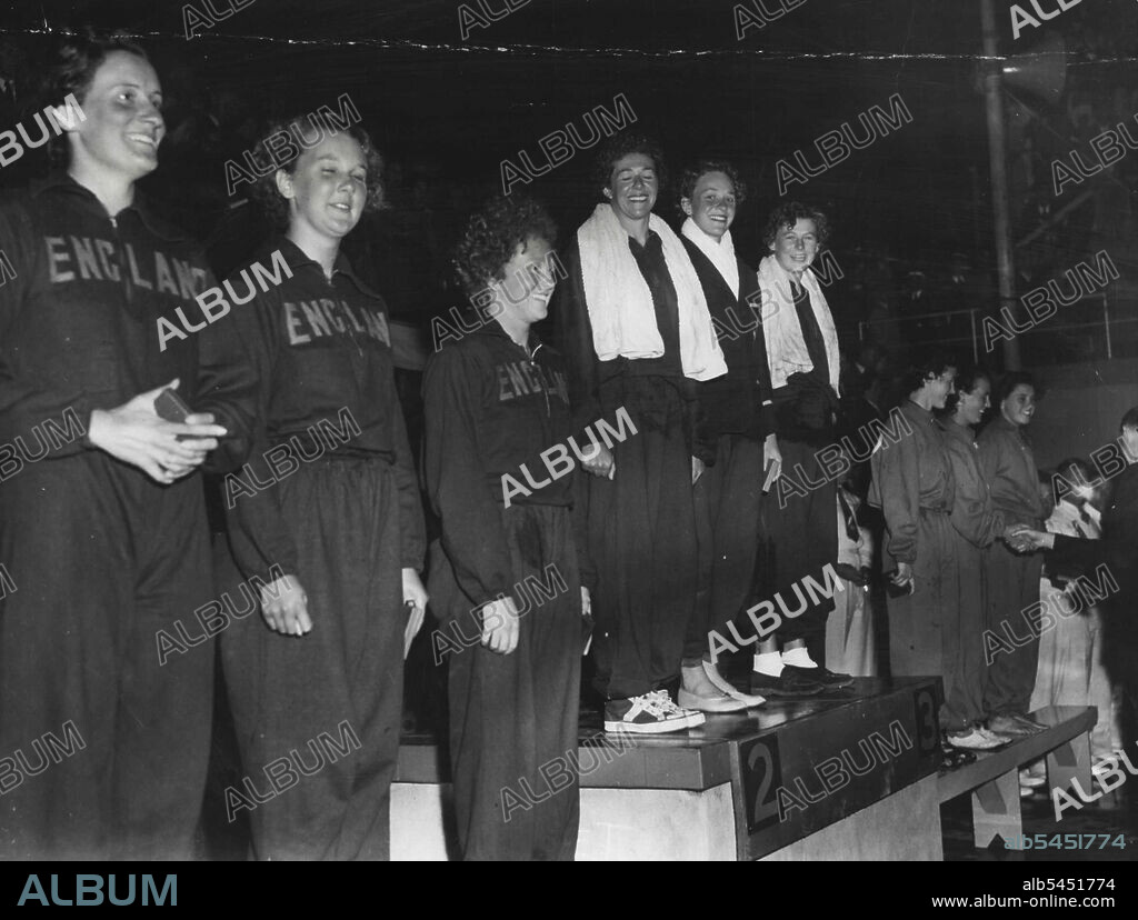 Relay race Games record - 3 minutes 53.8 secs. The "Victory Ceremony with the Australian team, winners of the 330 yards medley relay event, ***** Joy Davies, Nancy Lyons and Marjorie McQuade still laughing after the cocker spaniel incident (caption 4a). Nearest the camera is the English team (finished second) and furthest away the Scottish team (third). February 16, 1950.