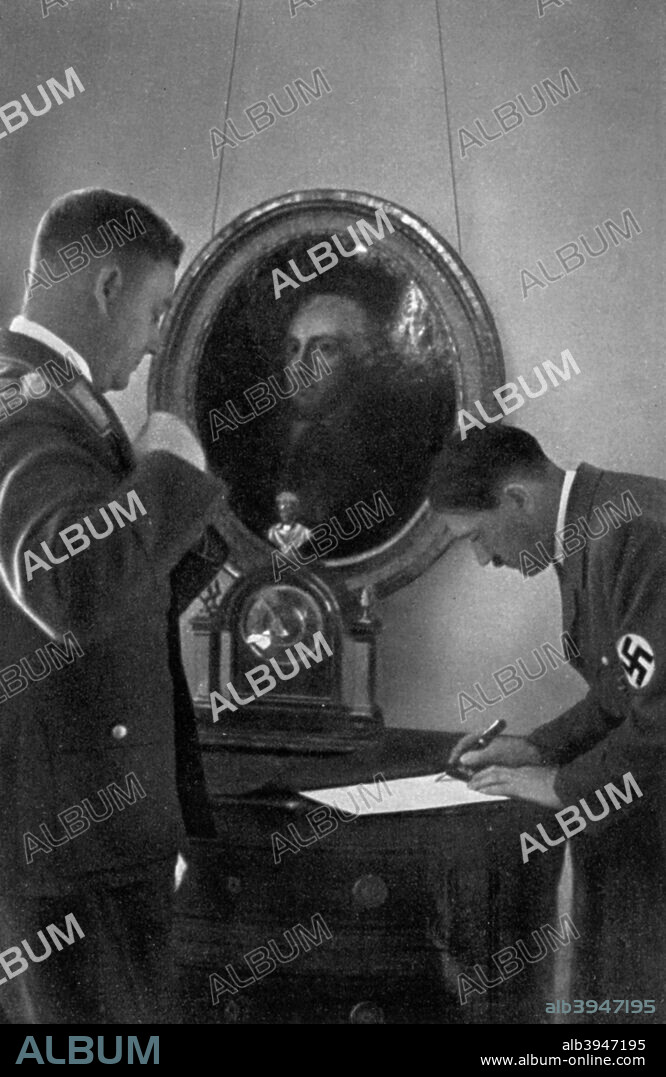 Adolf Hitler and Viktor Lutze, 1936. German Nazi leader Hitler (1889-1945) signing a document watched by Lutze (1890-1943), head of the Sturmabteilung (SA). Behind the two men is a portrait of Frederick the Great of Prussia (1712-1786). A print from Adolf Hitler. Bilder aus dem Leben des Führers, Hamburg: Cigaretten/Bilderdienst Hamburg/Bahrenfeld, 1936.