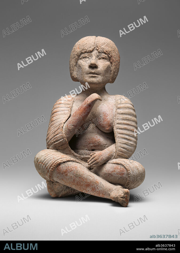 Female Figure. Culture: Xochipala. Dimensions: L. 5 1/2  x W. 3 7/8 x  D. 5 1/2 in. (14 x 9.8x 14 cm). Date: 15th-10th century B.C. (?).
This figure, made in the unusual Xochipala style, depicts a female seated with her legs crossed modeled in grey-colored clay. A full garment with horizontal stripes worked as evenly spaced grooves and a border indicated by fine incisions is draped around her body covering her shoulders and legs below her knees leaving her bare, full breasts and stomach visible. She raise one hand as if in mid-gesture. Her naturalistically rendered facial features with open eyes, large nose and thin closed lips show a serious expression. She has a full head of short hair indicated by striations parted in the center.