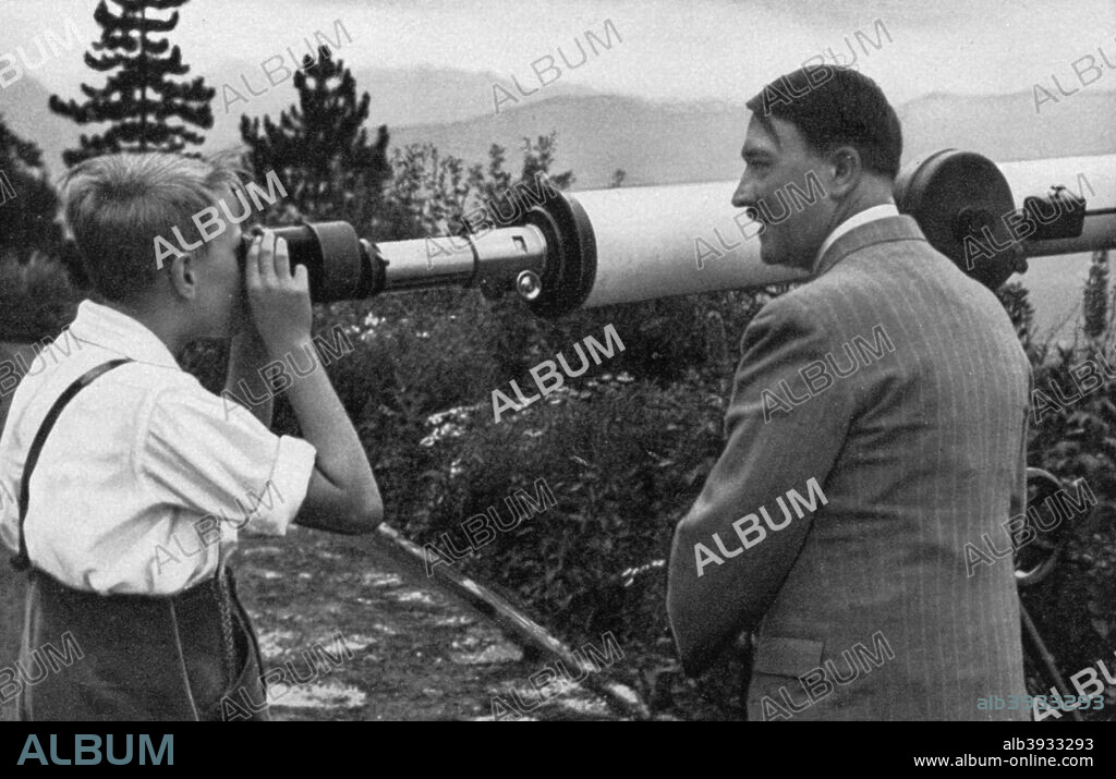 Adolf Hitler at his residence in Obersalzberg, Bavaria, Germany, 1936. Hitler (1889-1945) with a boy looking through a telescope at the Nazi leader's mountain rereat, the Berghof. A print from Adolf Hitler. Bilder aus dem Leben des Führers, Hamburg: Cigaretten/Bilderdienst Hamburg/Bahrenfeld, 1936.