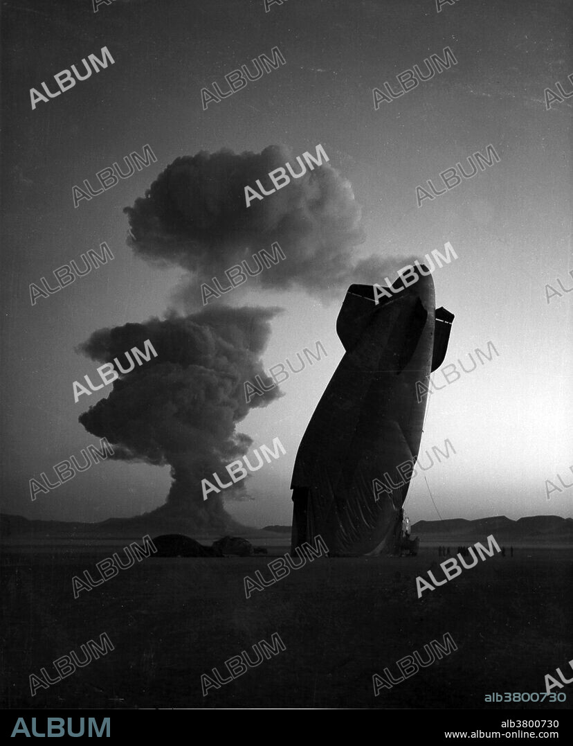 The tail section of a U.S. Navy Blimp is shown with the Stokes cloud in background. Blimp was in temporary free flight in excess of five miles from ground zero when collapsed by the shock wave from the blast. The airship was unmanned and was used in military effects experiments on blast and head. Navy personnel on the ground in the vicinity of the experimental area were unhurt. Stokes test of the LASL XW-30 multi-purpose warhead; used in TADM (tactical atomic demolition munition), and Talos SAM (surface-air-missile) warhead. All oralloy (highly enriched uranium) DT gas-boosted system. Balloon shot was detonated at 1500 feet on August 7, 1957. Operation Plumbbob was a series of nuclear tests conducted between May 28 and October 7, 1957, at the Nevada Test Site. It was the biggest, longest, and most controversial test series in the continental United States. The operation consisted of 29 explosions, of which only two did not produce any nuclear yield.