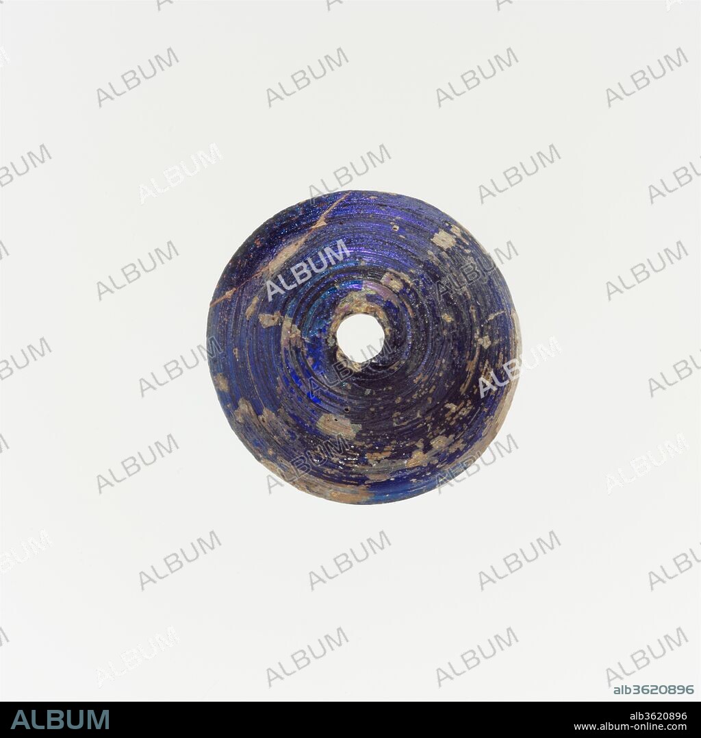 Glass spindle whorl. Culture: Roman. Dimensions: Diam. 1 in. (2.6 cm). Date: ca. 1st-2nd century A.D..
Translucent cobalt blue.
Domed body; flat bottom but with circular groove; vertical hole, larger on bottom.
Intact; pinprick bubbles; dulling, pitting, and iridescence, with patches of creamy weathering.
Made by winding trail in a spiral around rod.