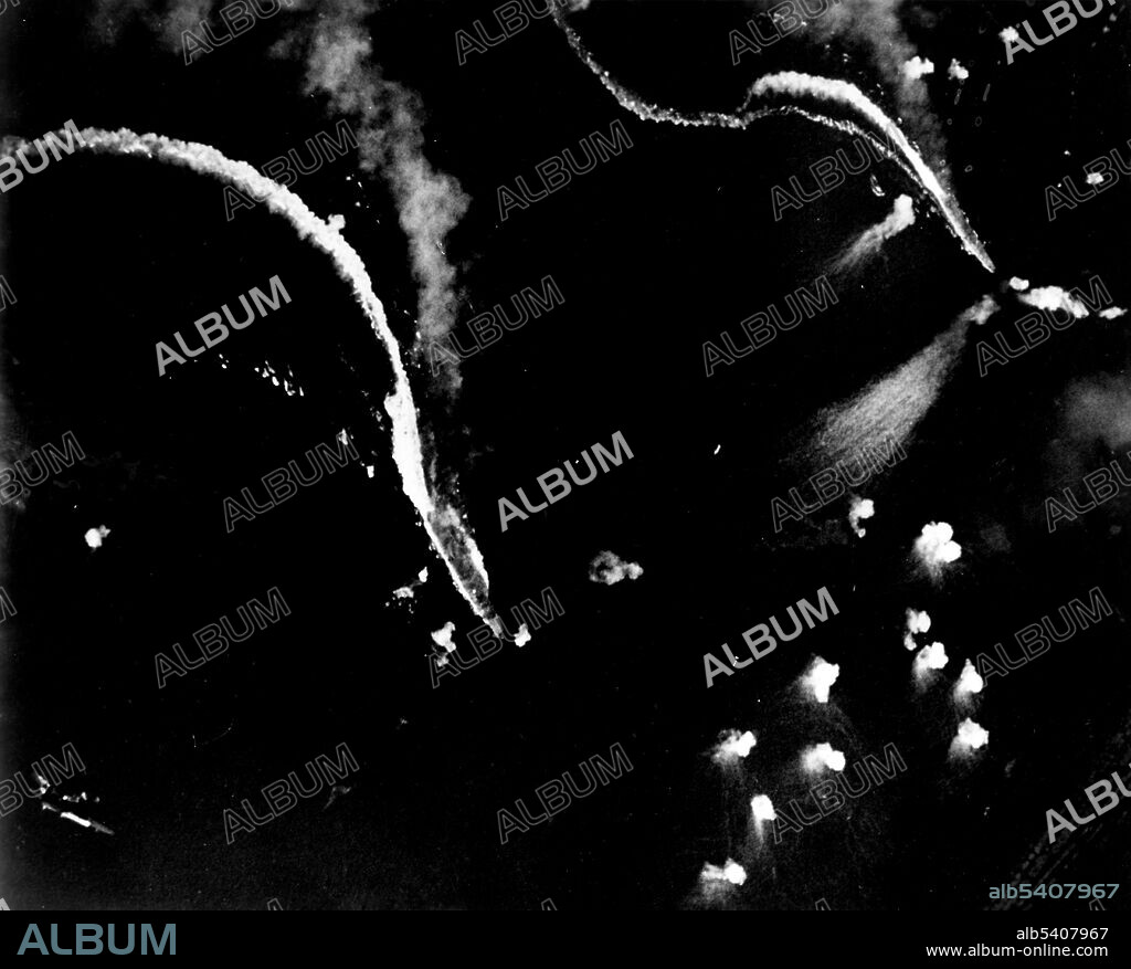 Japanese aircraft carrier Zuiho under attack by planes from USS Enterprise during the Battle off Cape Engano, October 25, 1944. Japanese aircraft carriers Zuikaku (left center) and (probably) Zuiho (right) under attack by U.S. Navy dive bombers during the Battle off Cape Engano. Both ships appear to be making good speed, indicating that this photo was taken relatively early in the action. Both carriers are emitting heavy smoke. Note heavy concentration of anti-aircraft shell bursts in lower right and right, and a SB2C Helldiver diving in the lower left. (cropped and cleaned).