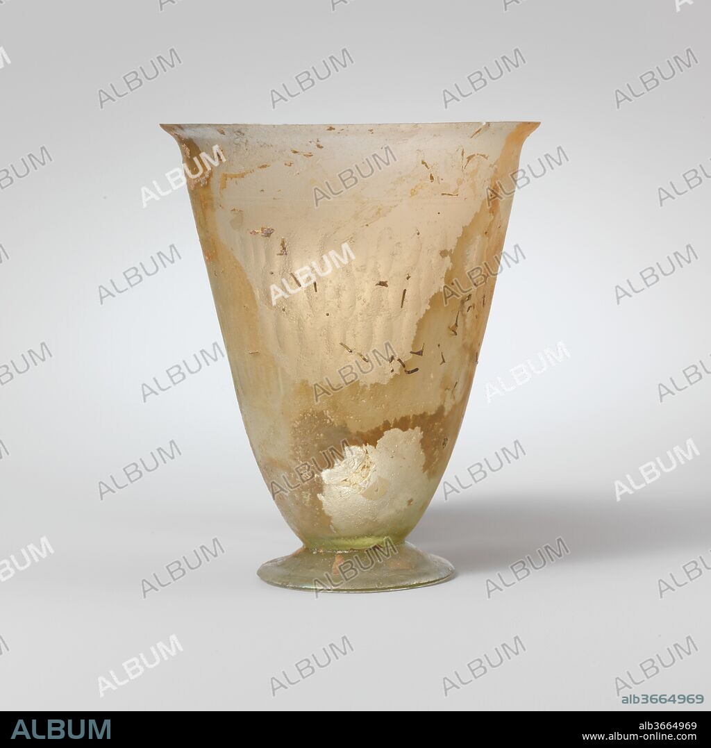 Glass beaker with facet-cut decoration. Culture: Roman. Dimensions: H.: 4 1/16 in. (10.3 cm)
Diam.: 3 1/16 in. (7.8 cm). Date: 2nd century A.D..
Colorless with light green tinge.
Thin, outsplayed, knocked-off rim; funnel-shaped body, tapering in at base; broad, low, conical, outsplayed foot, made from a separate paraison with a ground outer edge.
On upper body, two fine horizontal lines; below, broad band of four overlapping rice-shaped vertical facets, arranged in a slight irregular pattern.
Broken on one side of rim with part missing; pinprick bubbles; dulling, pitting, patches of brilliant iridescence, and creamy brown weathering.
Similar beakers have been excavated in Denmark, Germany, Egypt, and Afghanistan. The type must have been made at several localities around the Mediterranean.